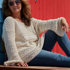 Woman sitting by a red door in the Bell Sleeve Sweater #115 in ecru