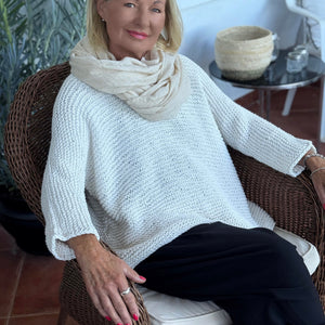 Vilja sweater #301 in white, worn with a cowl in a wicker chair