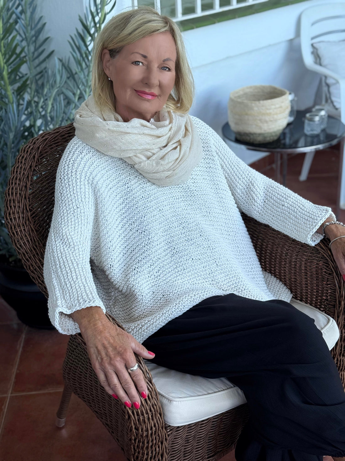 Vilja sweater #301 in white, worn with a cowl in a wicker chair