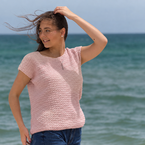 Woman by the sea wearing the Embla knitted t-shirt #132 in blossom pink