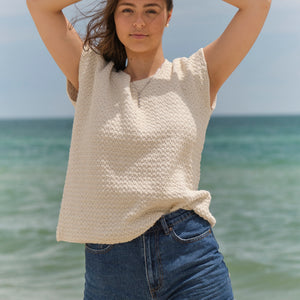 Woman on the beach wearing the Embla knitted t-shirt #132 in ecru with denim shorts