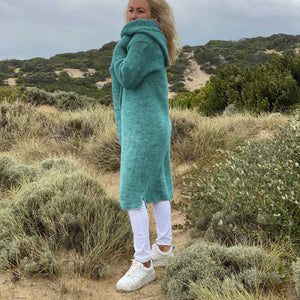 Elna hooded cardigan #133 in aqua, knitted in Scandi Soft XL and wrapped close against the wind on the dunes