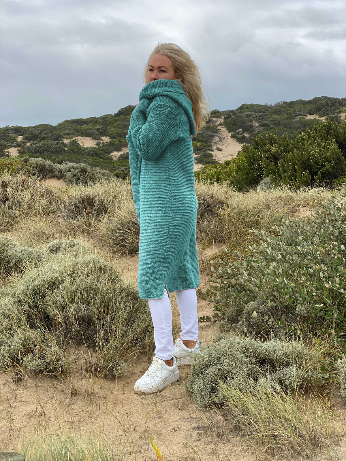 Elna hooded cardigan #133 in aqua, knitted in Scandi Soft XL and wrapped close against the wind on the dunes