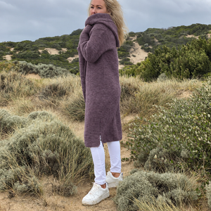 Elna hooded cardigan #133 in grape, a long oversized knit worn with white jeans and trainers by the sea