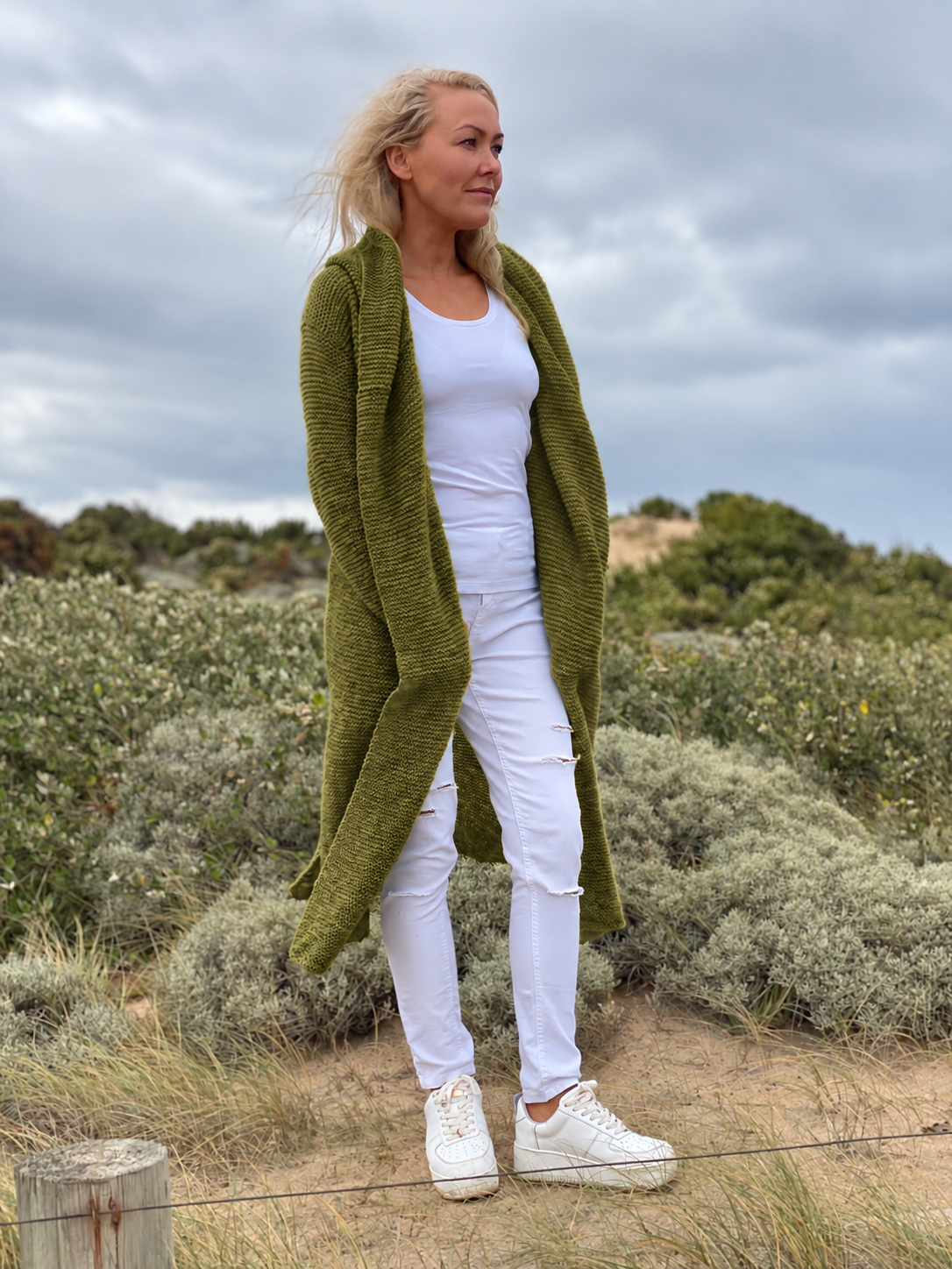 Elna hooded cardigan #133 in olive, worn open over a white top to show the long garter stitch fronts