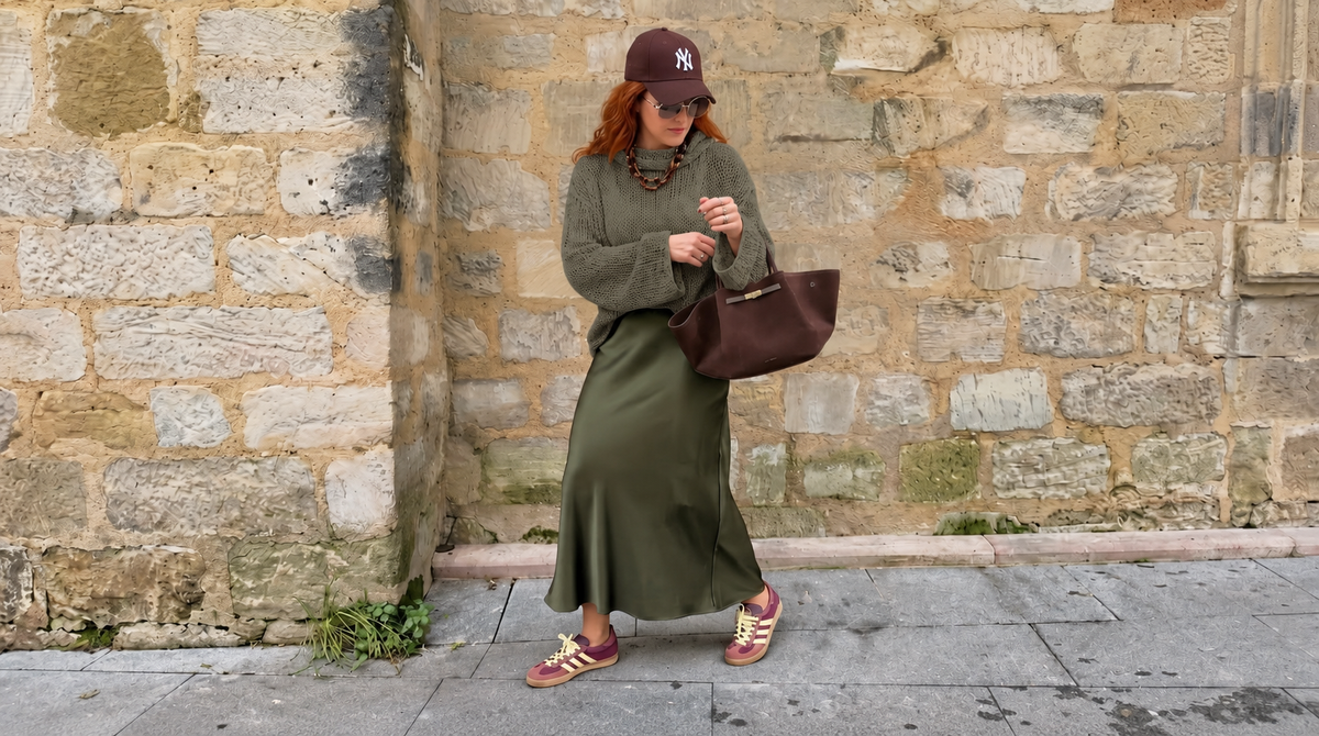 Tora Loose Sweater #141 in eucalyptus, worn over a long green skirt by a stone wall