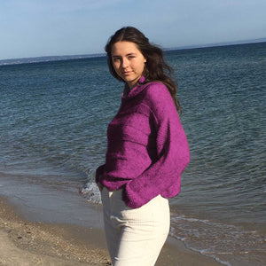 Woman on the beach wearing the Runa Icicle Sweater #145 knitted in Scandi Soft XL Wild Berry