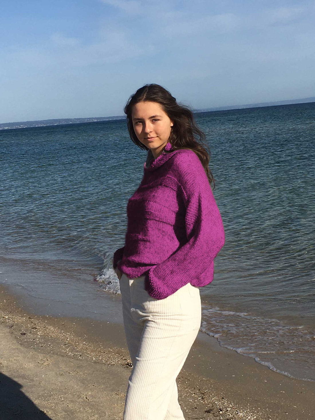 Woman on the beach wearing the Runa Icicle Sweater #145 knitted in Scandi Soft XL Wild Berry
