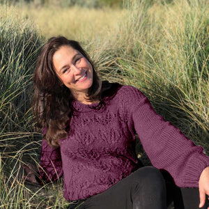 Woman sitting in dune grass wearing the Ingrid lace jumper #149 in grape