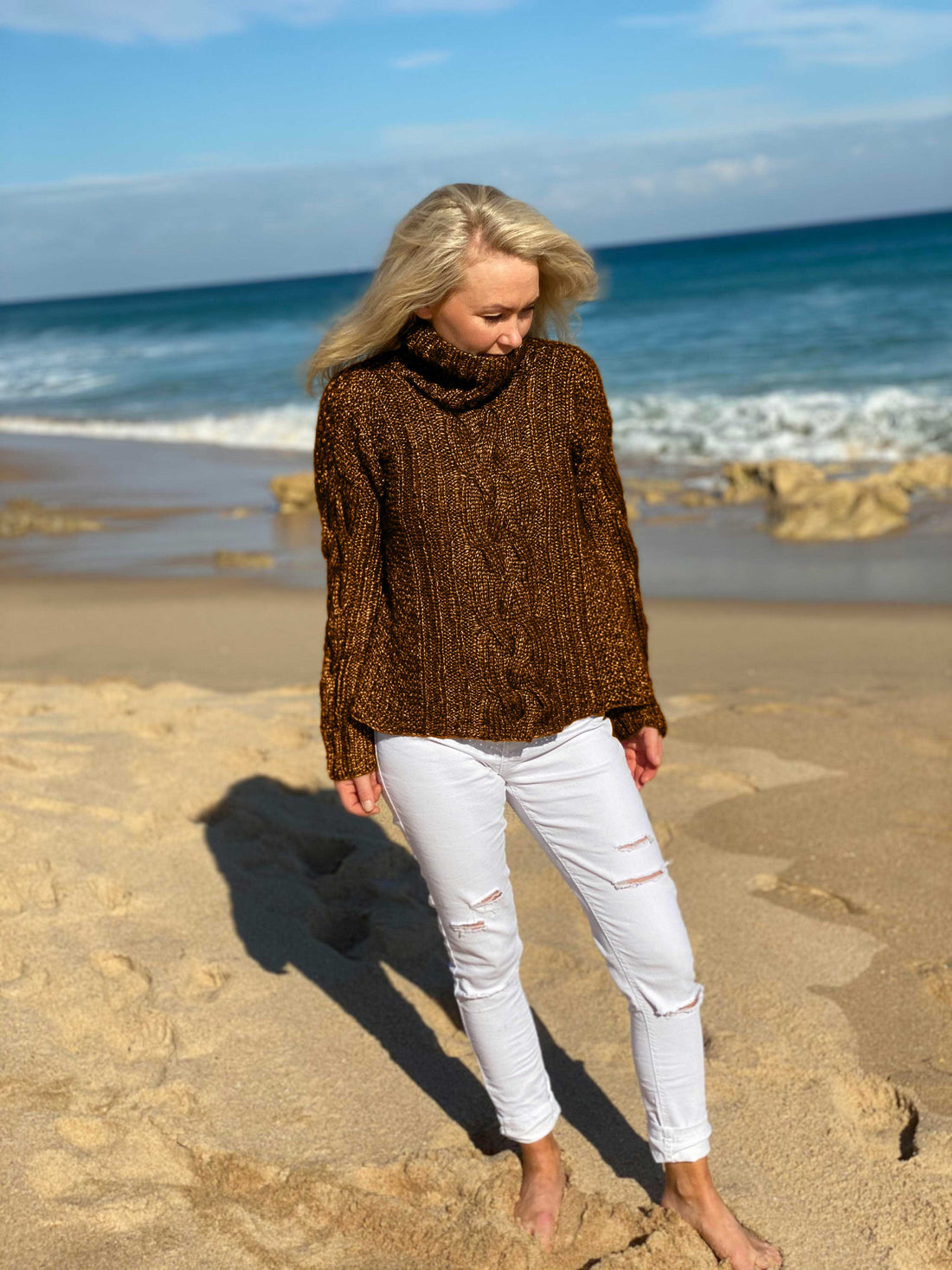 Woman on the beach wearing the Hedda Cable Roll Neck #150 knitted in Scandi Wool Toffee