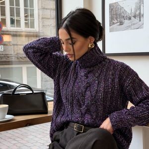 Hedda Cable Roll Neck #150 in amethyst, worn seated in a café with dark trousers