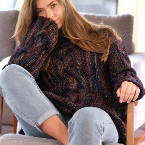 Hedda Cable Roll Neck #150 in black rainbow, worn curled up in an armchair
