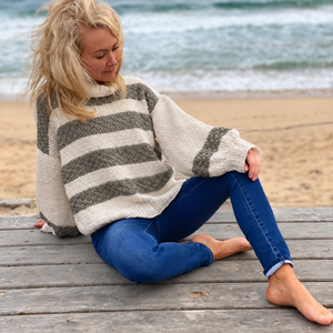 Svala Striped Sweater #182 with eucalyptus stripes, worn sitting on a boardwalk by the sea