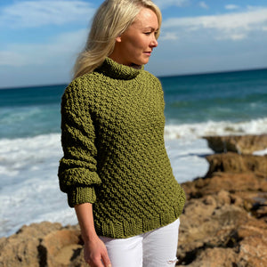 Woman wearing the Classic Roll Neck sweater #185 in olive with white trousers