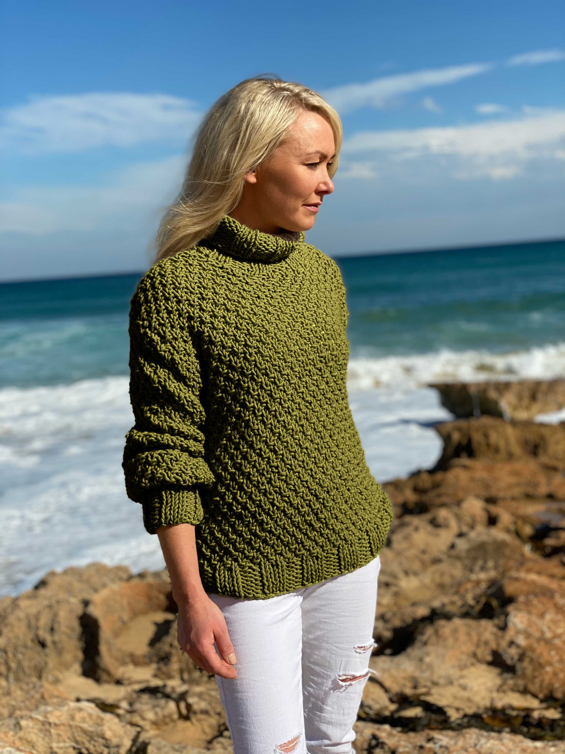 Woman wearing the Classic Roll Neck sweater #185 in olive with white trousers