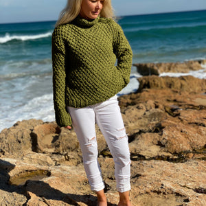 Woman standing on rocks by the sea in the Classic Roll Neck sweater #185 in olive