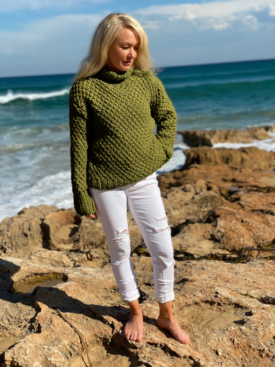 Woman standing on rocks by the sea in the Classic Roll Neck sweater #185 in olive
