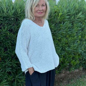 Vilja One Size Sweater #301 in white, a loose V-neck in garter stitch worn in a garden