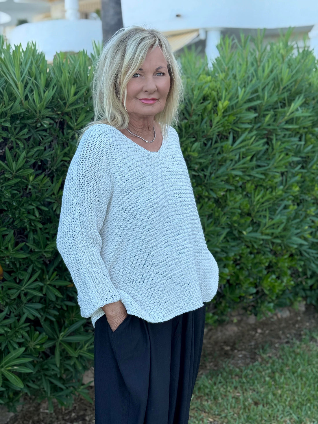 Vilja One Size Sweater #301 in white, a loose V-neck in garter stitch worn in a garden