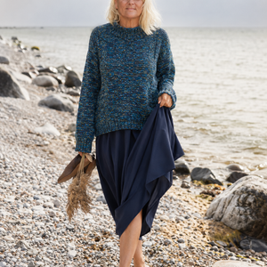 Nova Basic Sweater #304 in turquoise, worn with a long skirt on a pebble beach
