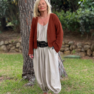 Super Easy Cardigan #316 in terracotta, worn open over a cream top and linen trousers in a garden