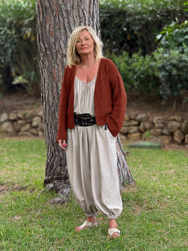 Super Easy Cardigan #316 in terracotta, worn open over a cream top and linen trousers in a garden