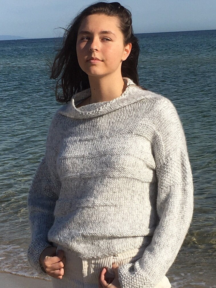 Runa Icicle Sweater #145 in ice, worn by the sea with the tall collar folded down