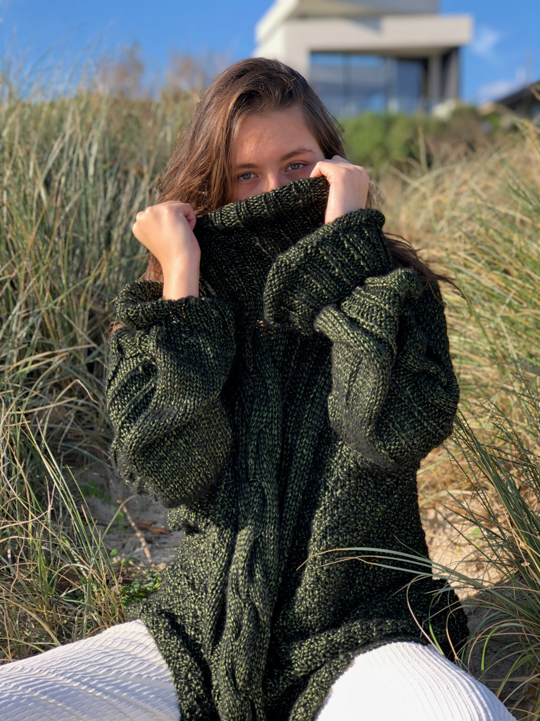 Hedda Cable Roll Neck #150 in forest green, with the deep ribbed collar pulled up in the dunes