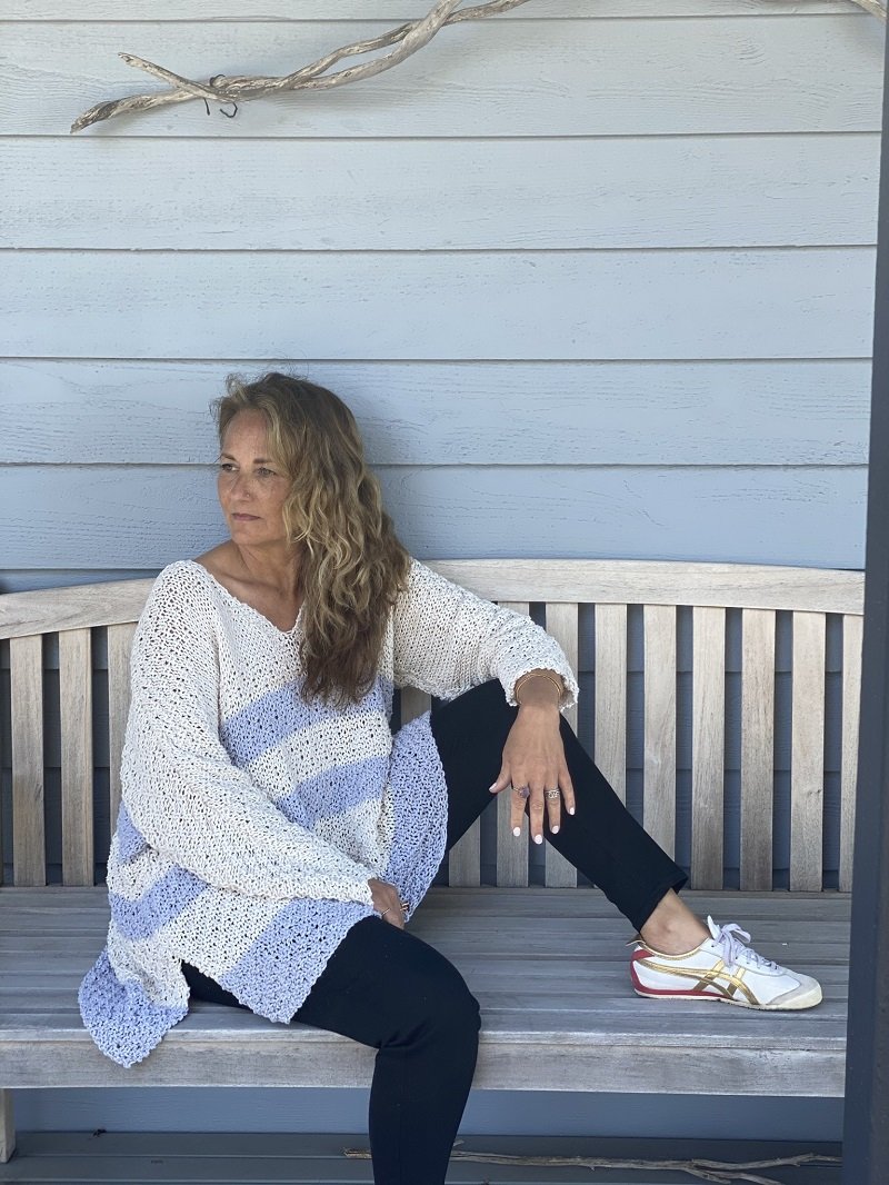 Woman sitting on a bench wearing the Serenity two-colour sweater #166 in white and pale blue