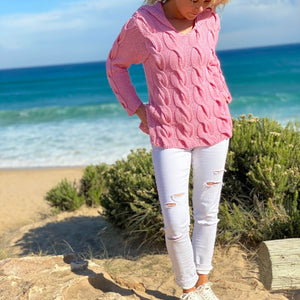 Woman on a dune path wearing the Hooded Cable Jumper #172 in pink with white trousers