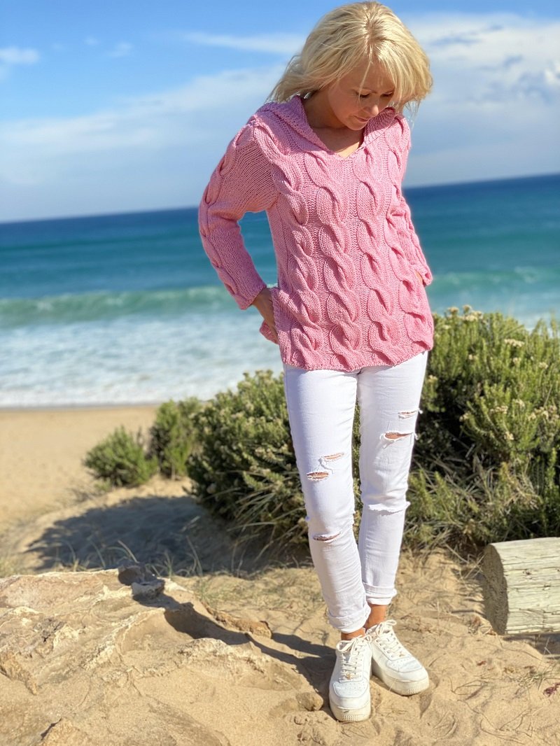 Woman on a dune path wearing the Hooded Cable Jumper #172 in pink with white trousers