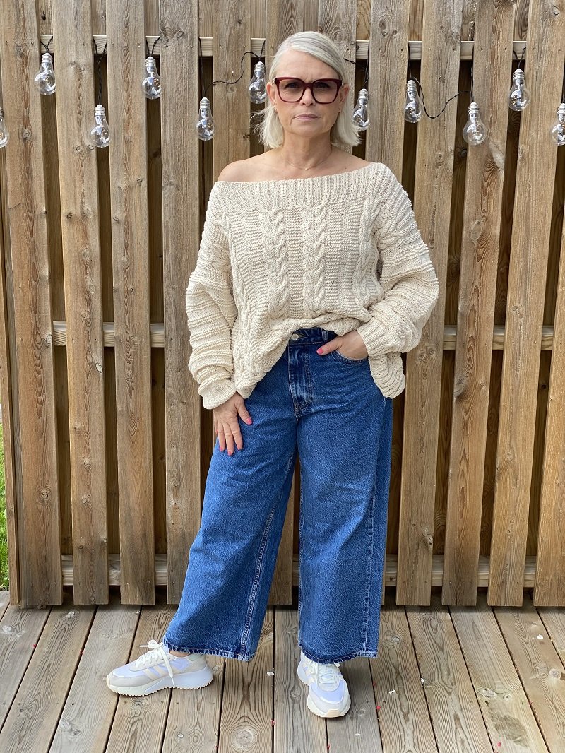 Woman wearing the Elisabeth cable jumper #113 in ecru with wide blue jeans