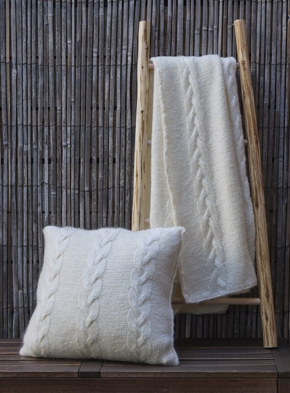 The Cable Cushion and Throw set #205 in cream, the cushion propped against a ladder with the throw